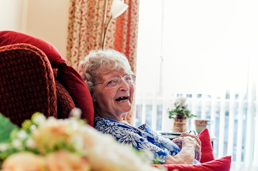 An older woman in an armchair smiling at the camera.