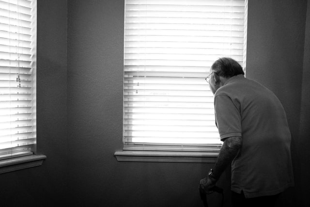 A black and white photograph of an old man looking out the window. 