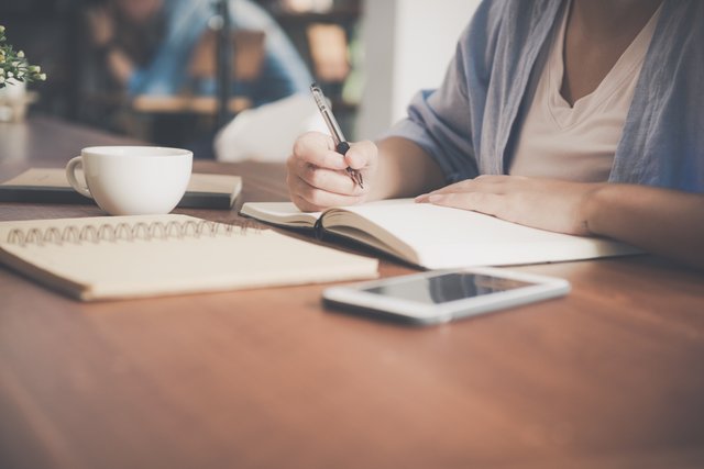 A woman writes in her journal with a coffee. 